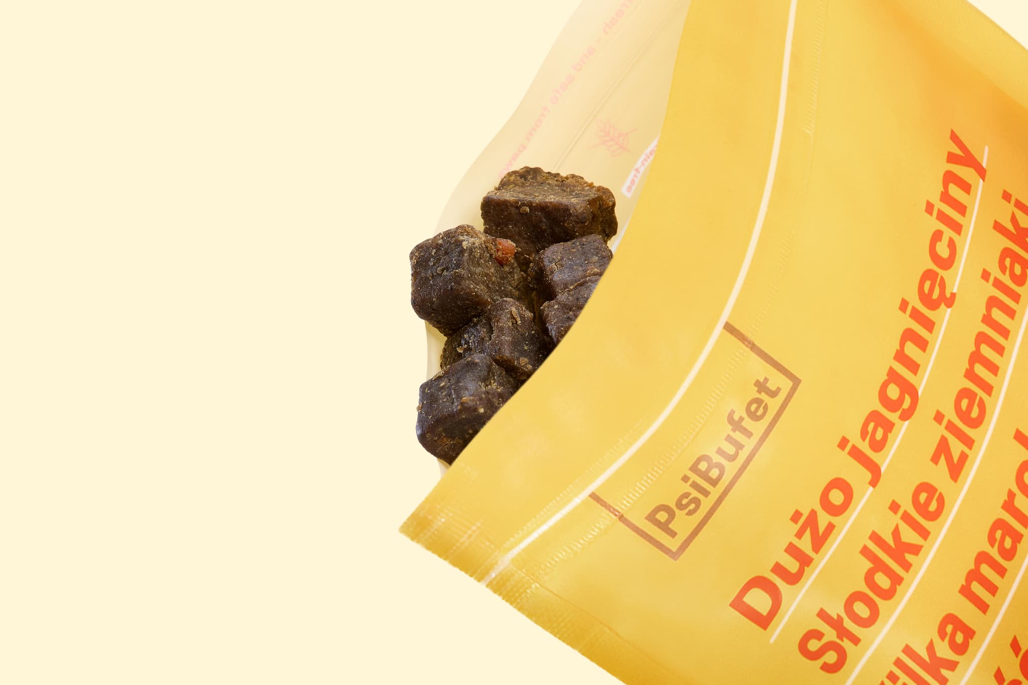 A yellow PsiBufet package partially open, revealing dark brown, chunky treats. Polish text written vertically on the package.